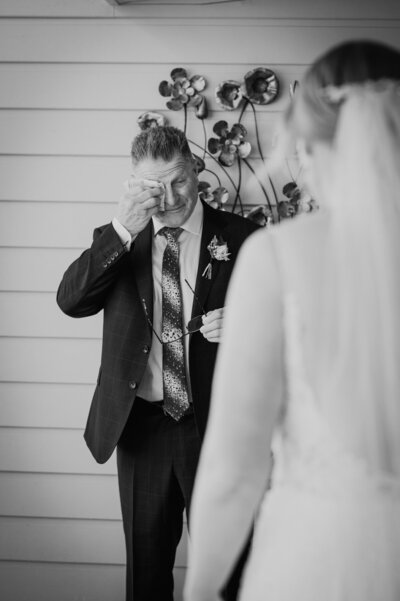 Father of the bride wiping tears as he sees his daughter in her wedding dress