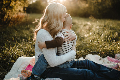 a mother smiles as she hugs her toddler son during family photos