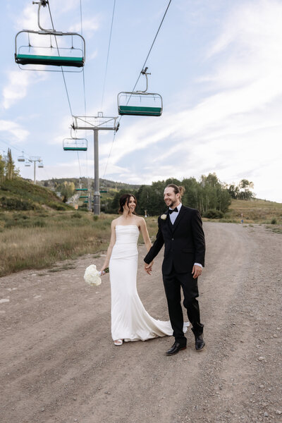 A bride and groom holding hands and walking down the ski hill together in Aspen, Co on their wedding day.  Photo taken by Kelly Elizabeth Photography.