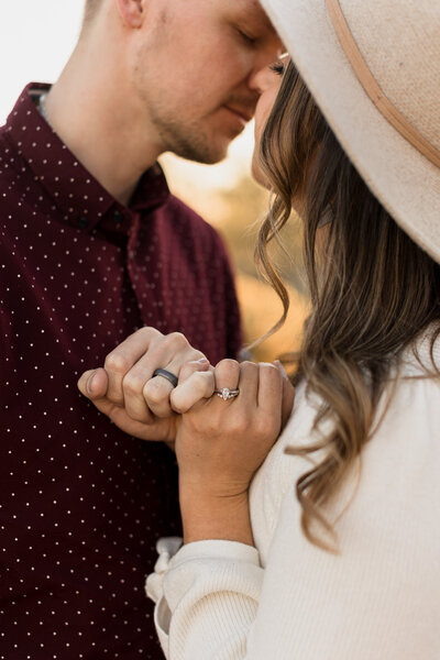 Image of a couple showing off their wedding rings by pinky promising while leaning in for a kiss