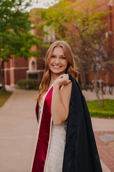 girl poses with cap and gown for graduation photos in dallas texas