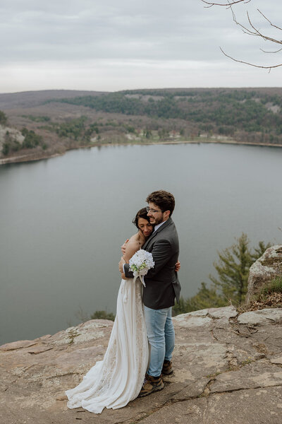 bride and groom embracing on an overlook over a lake at Devil's Lake State Park