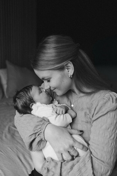 Tijdens een newbornshoot knuffelt de mama haar pasgeboren dochter met een liefdevolle lach op haar gezicht.