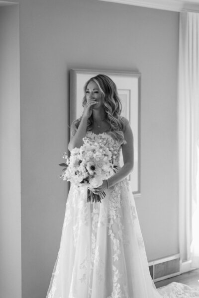 A bride looks into a mirror and sees herself for the first time as a bride. The photo is black and white and shows the emotion as the bride holds back tears. 