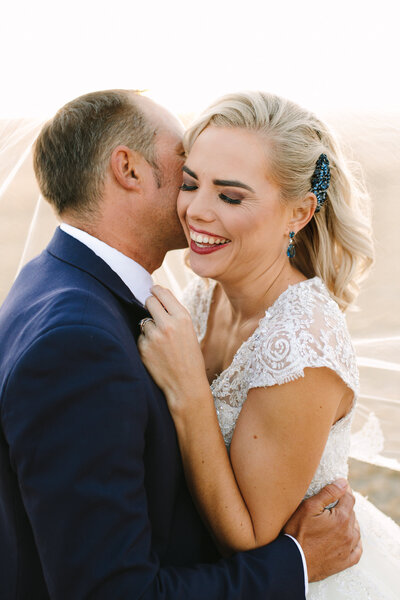 The bride bursts into joyful laughter, clutching her groom’s jacket as he makes her laugh on their wedding day, both radiating happiness; a candid moment beautifully captured by a wedding and elopement photographer based in Bendigo, Victoria.