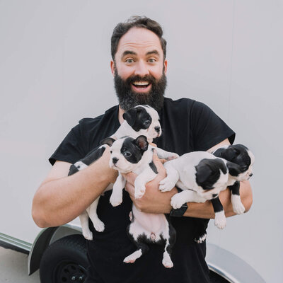 Ryan Erickson, owner of Fetch Photo Truck holding four puppies excitedly in front of his trailer