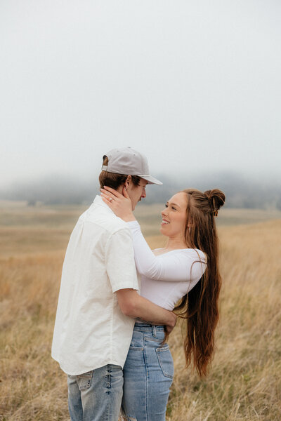 A girl holding her fiances face as she smiles at him at their portrait session.