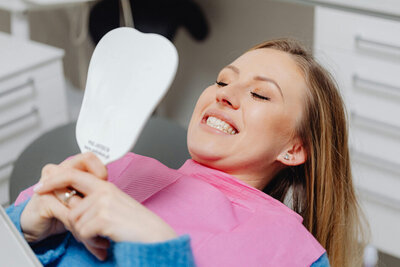 Dentist office Middleton Idaho. A woman is sitting in a chair looking into a mirror and smiling, checking her teeth.