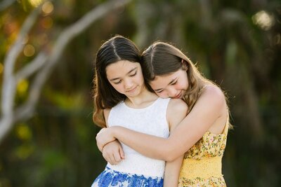 Two young girls hug on a beach.