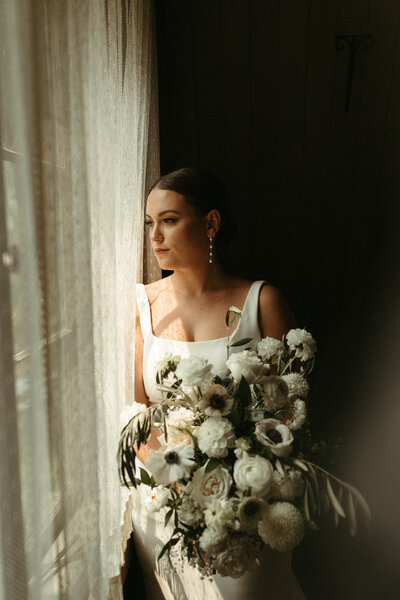 Bride standing by window with fairytale florals and pearl earrings.