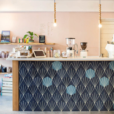 Coffee bar with blender , and grinder on top. The wall is light pink with the menu hand painted in  black on the wall- Romero Album Design