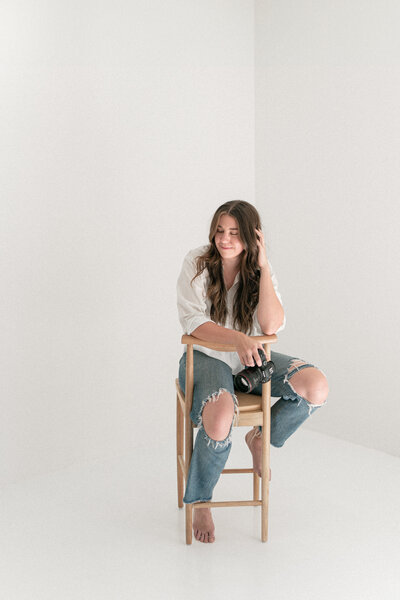portriat of nicole sitting backwards on a wooden stool in an all-white studio