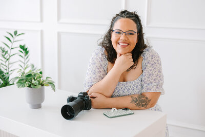 A person leaning on a table with their hand under their chin smiling