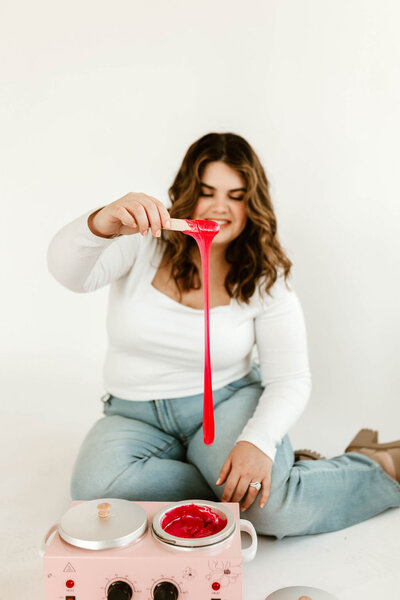 Licensed esthetician Macayla Hopper holding wax stick over wax warmer during body waxing prep in Hartselle studio