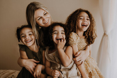 A mom and her three mixed race children snuggling together and laughing with one another at a boho photography studio in fort worth, texas