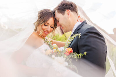 Bride and groom under brides veil at their wedding in Littleton, Colorado at the Arrowhead Golf Course featuring beautiful colorful bouquet.
