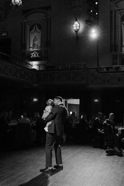 A person holding a small baby and dancing at a wedding 