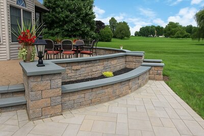 Hardscape design showcasing curved stone retaining walls, paver flooring, and outdoor dining setup.