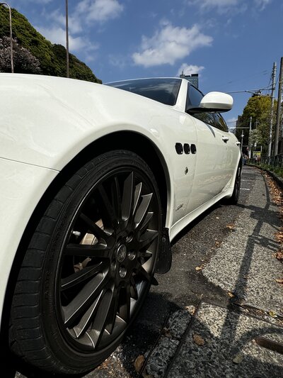 Close-up of the Maserati Quattroporte’s front wheel and grille, captured during a Tokyo Luxe Drive experience on a scenic road.