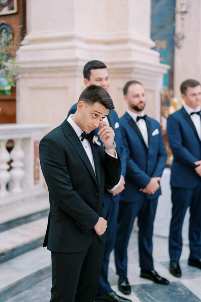 Groom wiping away a tear as he sees the bride walking down the aisle, elegant church ceremony in classic style