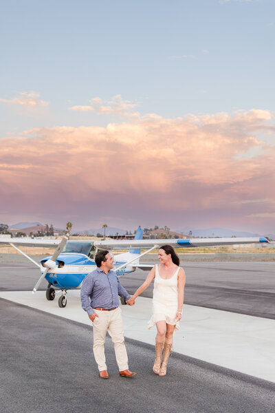 engaged cuple walking in front of airplane