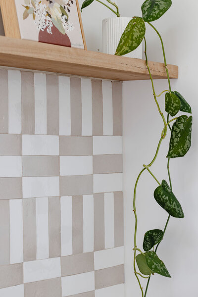 A potted plant with vine trails elegantly down a wooden shelf, complementing the checkered beige and white wall, showcasing the bespoke touch of custom interior design Newcastle.