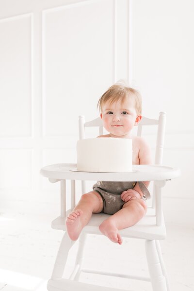 one year old baby boy sits in high chair with his first birth cake during studio portrait session in charlotte nc