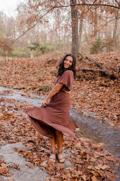 Teen girl captured by the camera mid-twirl in the autumn leaves.