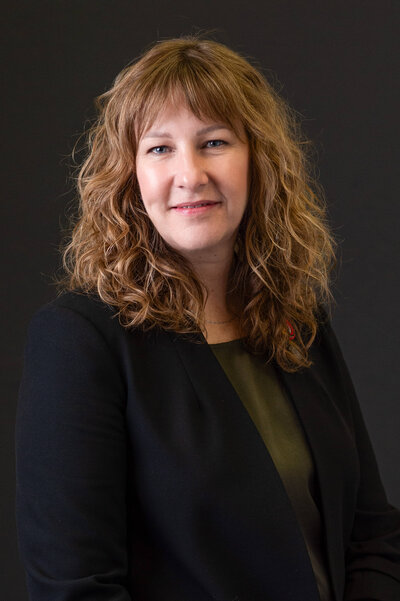 a corporate headshot of a woman in a blue suit and green sweater against a black backdrop.  Captured by Ottawa Event Photographer JEMMAN Photography COMMERCIAL
