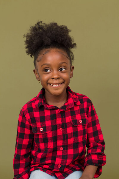 Portrait of a young black girl on a olive backdrop. Coy smile.