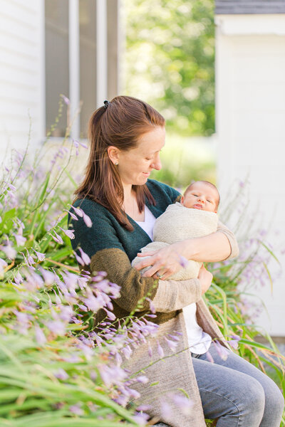 mother holding newborn baby outside house with purple flowers