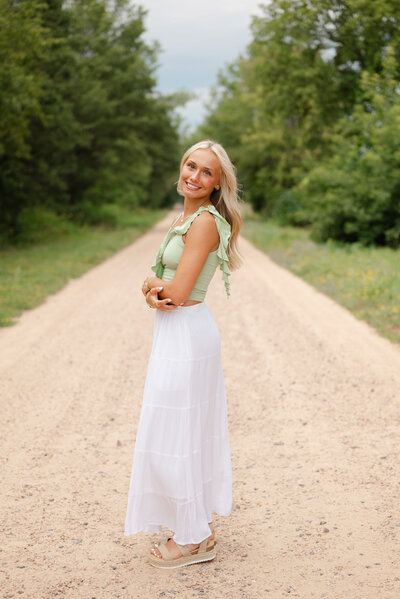 A confident high school senior girl smiling at the camera, standing outdoors. 