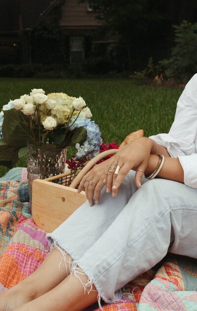 Woman sitting on a colorful blanket next to a basket and a vase of flowers 
