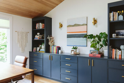 A blue credenza with potted plants sitting on top and a colorful painting hanging above it, representing a paint color consultant.