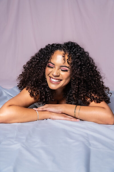 Woman with curly hair smiling with her eyes closed.