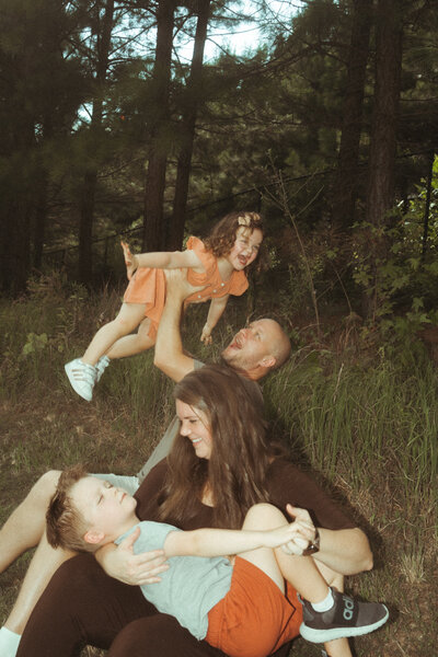 A family of four sitting in the grass at Noonday Creek Trail and playing with each other. 