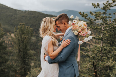 Bride hold flowers stands on a hill with groom in the background