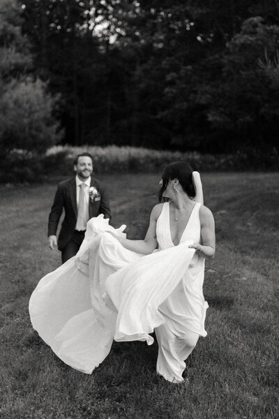 Bride and groom running through a field while smiling at each other