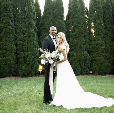 Bride and groom pose with a lush floral bouquet 