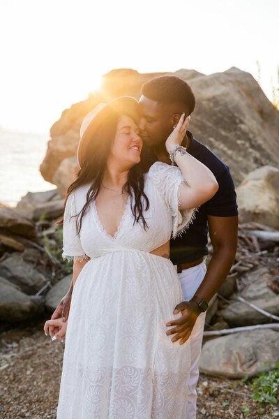 Bride and groom sharing a romantic dip kiss in front of a rustic barn, with the groom holding a bouquet of flowers and the bride's dress trailing behind her