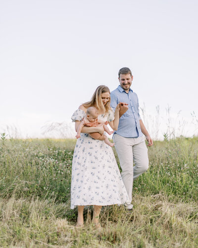 Mom holds young baby and holds hands with her husband during family portrait session