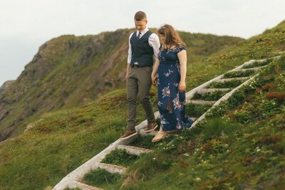 bride and groom walk down wooden steps on the side of a cliff in Newfoundland