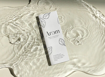 Carton d'emballage pour huile essentielle avec identité visuelle Arôm entouré d'eau. Crée par le Studio Youmé, spécialiste en identité de marque en Vendée.