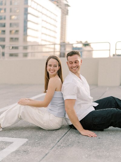 Emily and Nate back to back sitting on parking garage roof