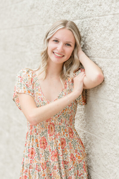 senior girl in ludington standing against wall with arm up by head