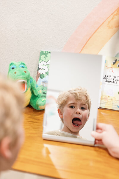 Young patient practicing Orofacial Myofunctional Therapy exercises in front of a mirror.