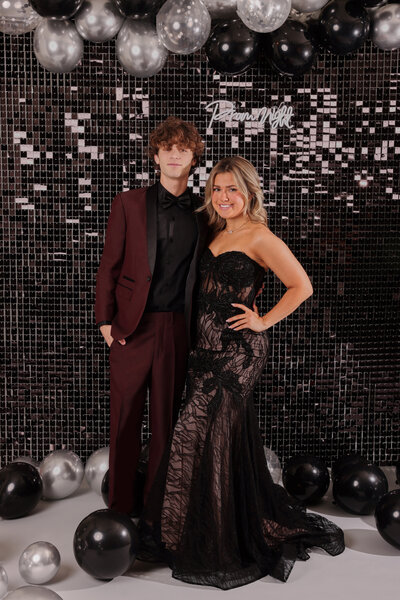 A boy wearing a red high school prom suit with his date wearing a black prom dress