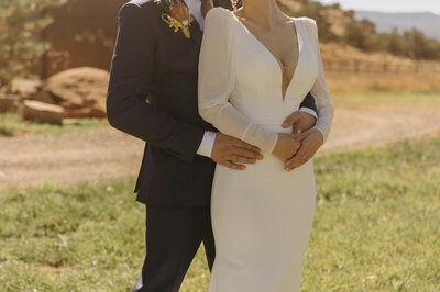 A groom holding the waist of his bride. She is standing in front of him, slightly to the right. The photo is from the neck down so you cannot see their faces.