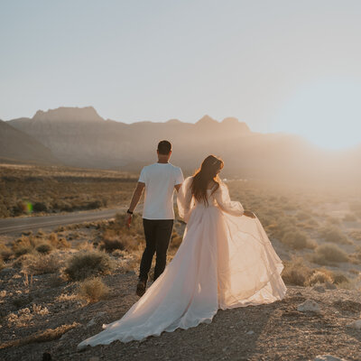 a couple who just renewed their vows in red rock canyon in las vegas nevada walks in front of their photographer in a gorgeous wedding dress