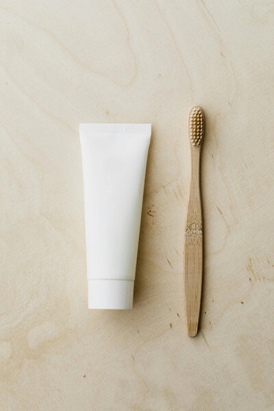 A wooden toothbrush used for cleanings and a white tube of toothpaste laying on a beige countertop.